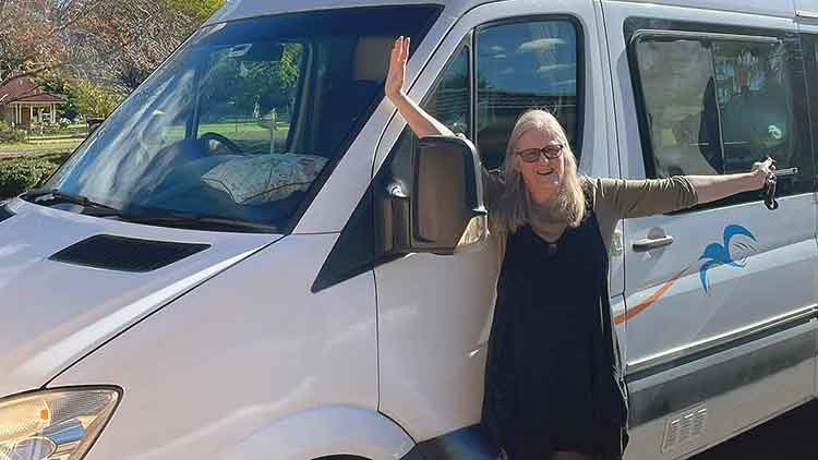 Lesley standing against her RV with her hands in the air from excitement.
